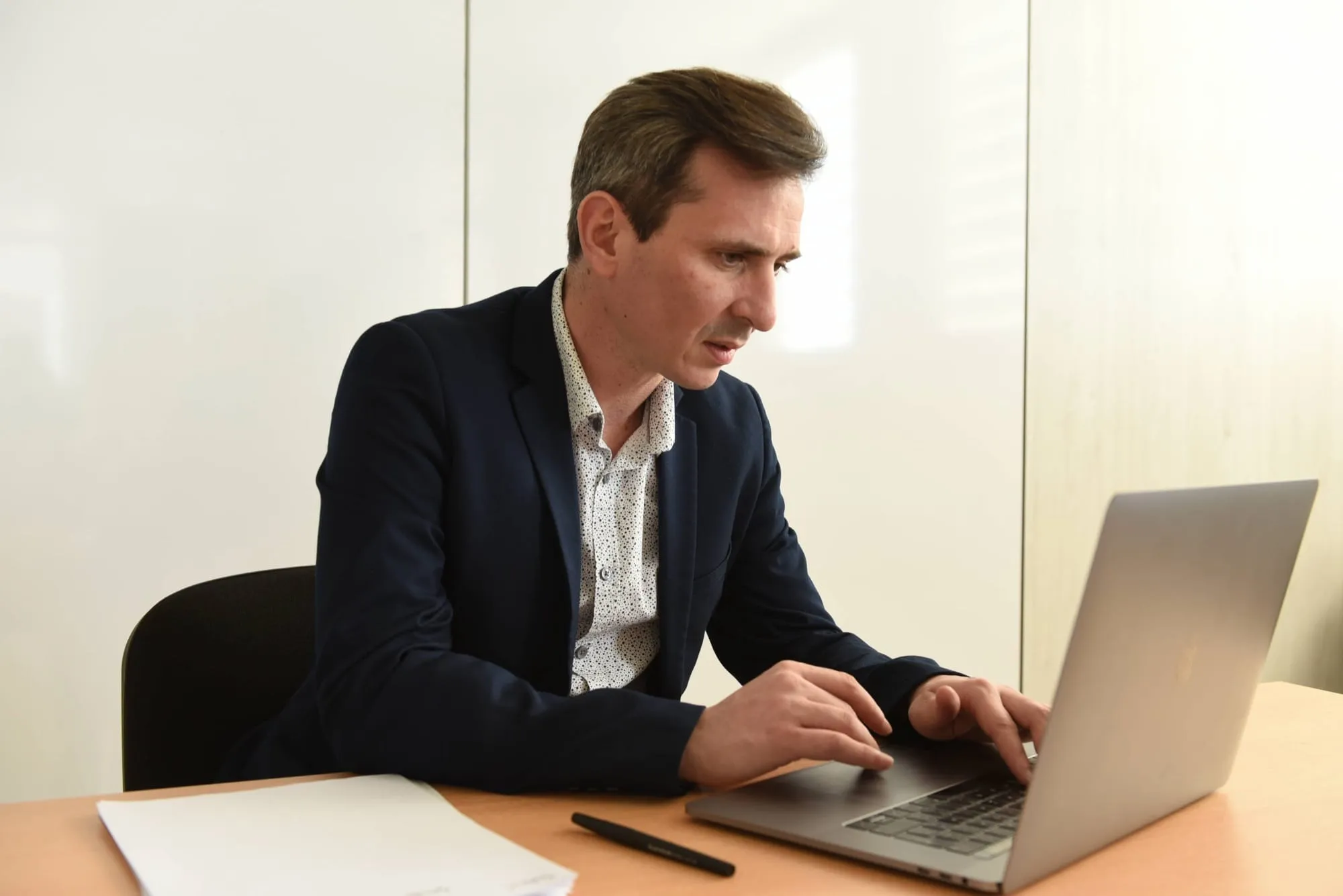 Jérémy Sarda, en veste bleu nuit, concentré sur son ordinateur portable à son bureau.